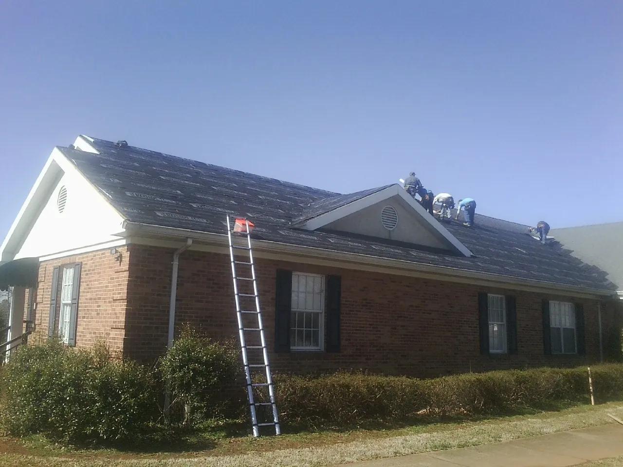 Crew tearing shingles off a brick ranch roof with a ladder set — Metal Roof Repair work by our crew in Gales Creek