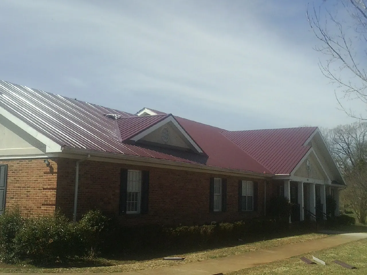 Red metal roof with gabled entries on a long brick building, from a Hail Damage Roof Repair job in Gales Creek
