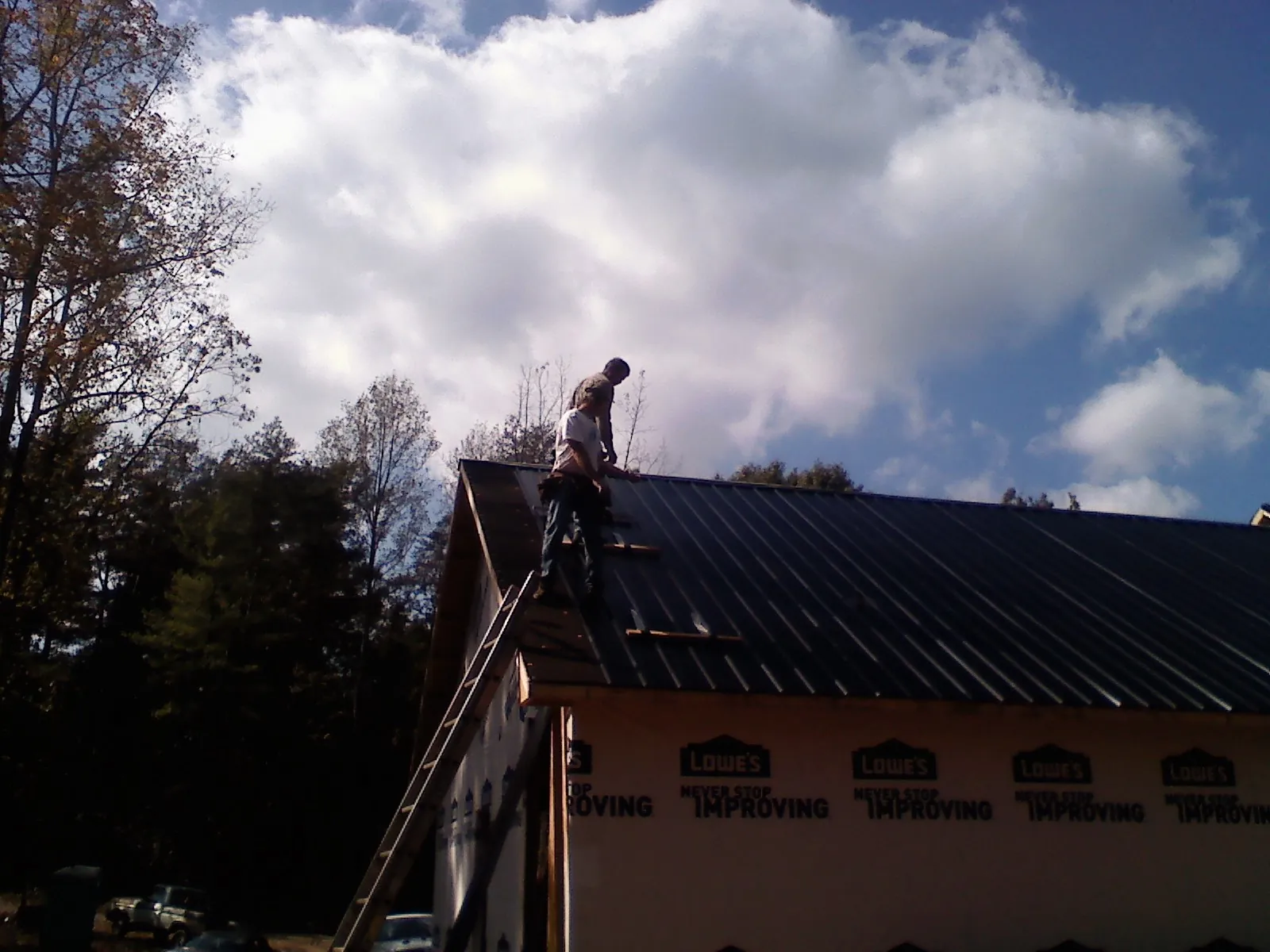 Roofer fastening dark metal panels high against a cloudy sky, from a Roof Inspection job in Gales Creek