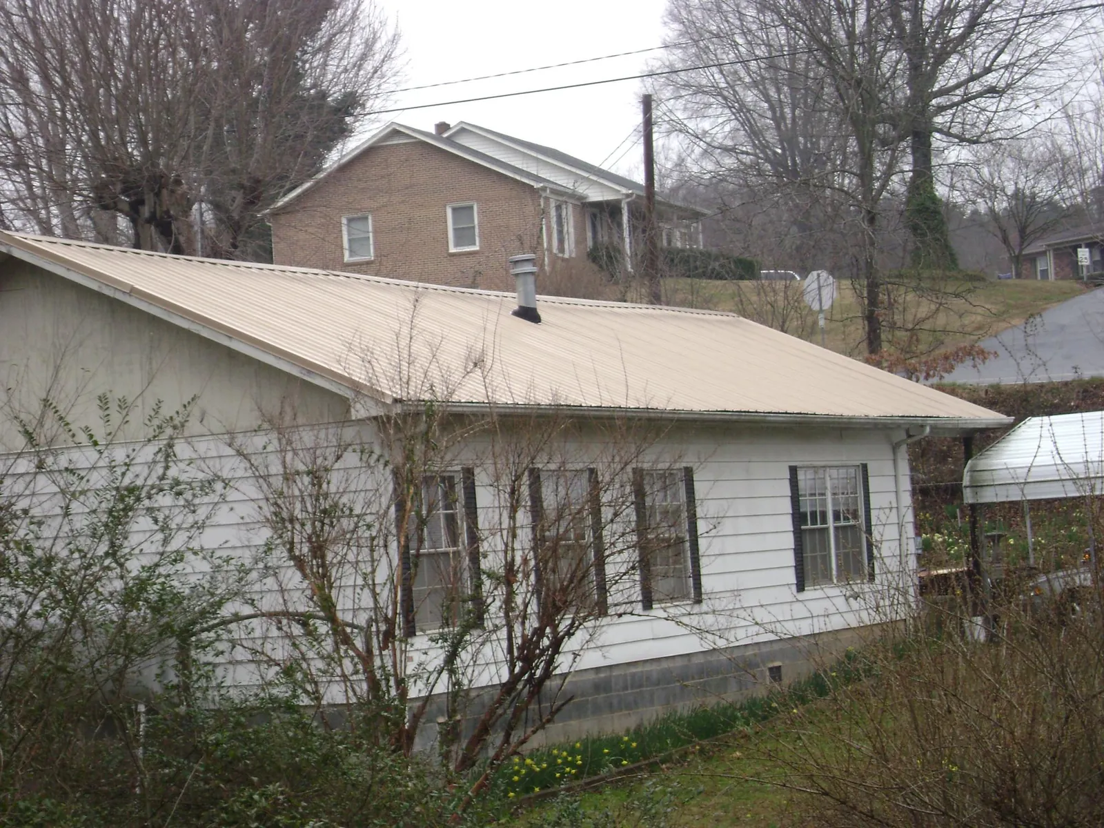 Tan metal roof on a white sided house set into a hillside — Commercial Roofing by Roofing Brothers in Gales Creek