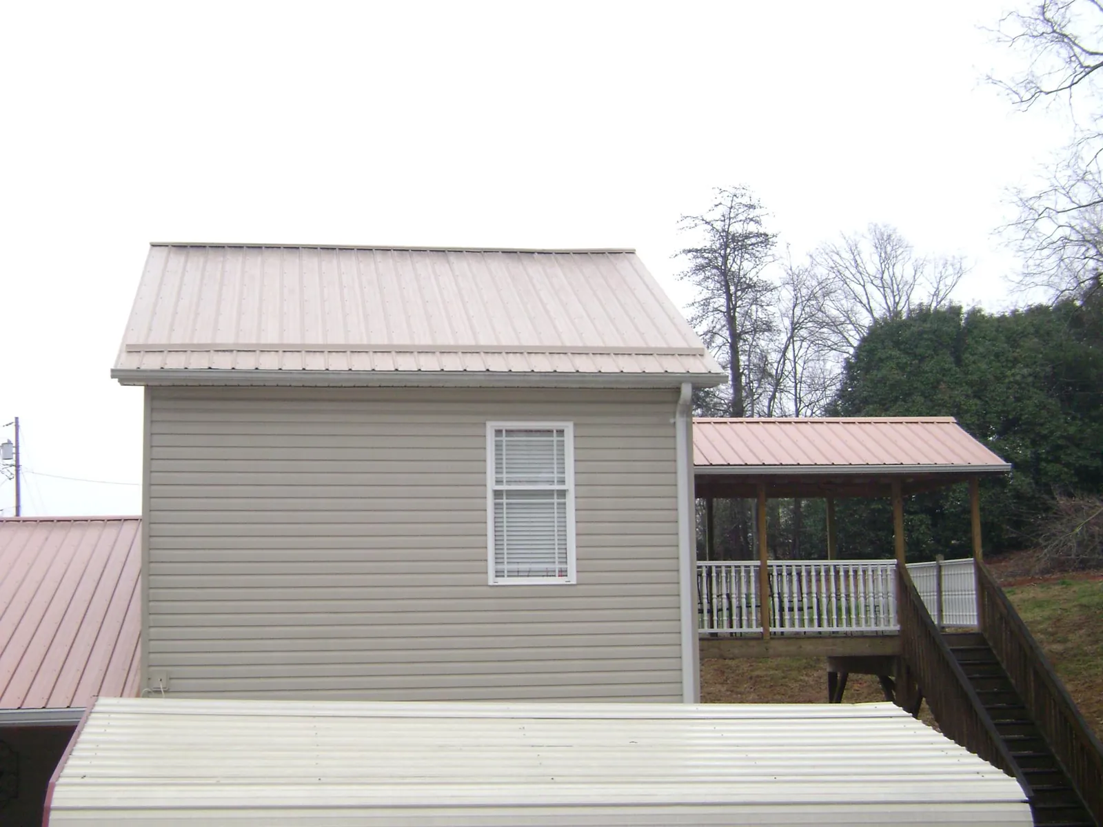 Tan metal roofs on a two story addition and attached porch, from a Roof Replacement job in Gales Creek
